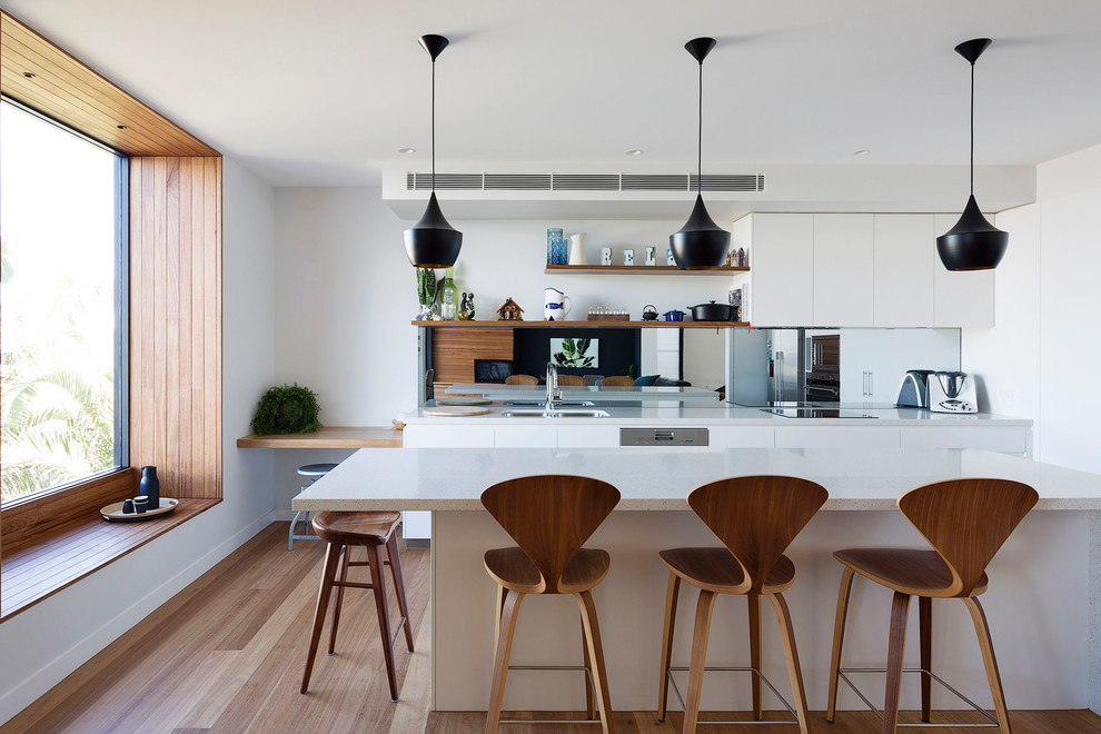 Design ideas for a contemporary l-shaped eat-in kitchen in Sydney with an undermount sink, flat-panel cabinets, white cabinets, mirror splashback, stainless steel appliances, medium hardwood floors, with island, brown floor and white benchtop.