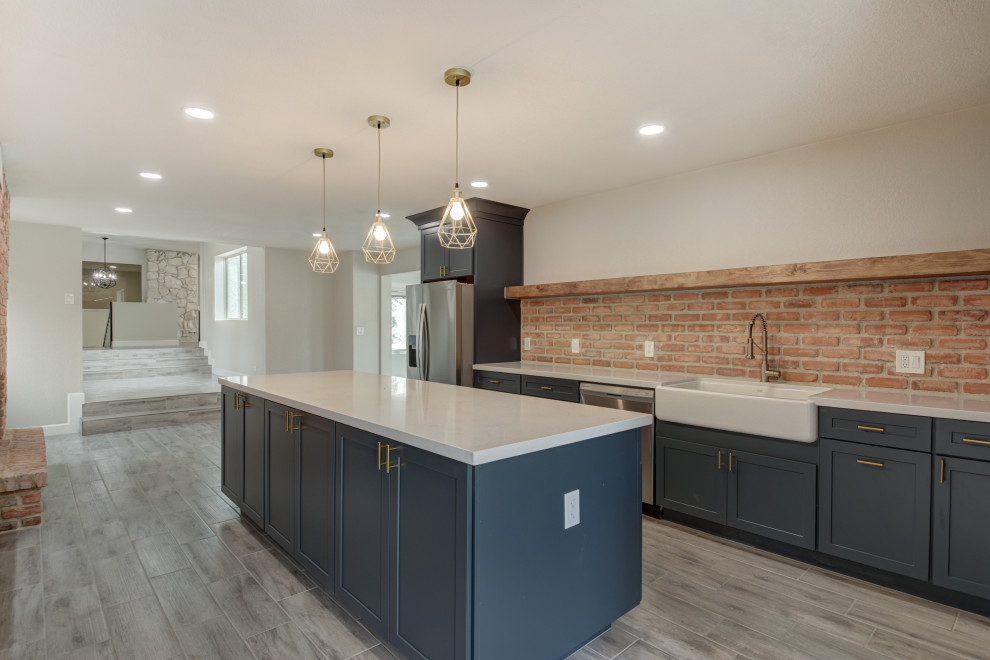 Inspiration for a mid-sized transitional u-shaped porcelain tile and gray floor eat-in kitchen remodel in Phoenix with a farmhouse sink, shaker cabinets, blue cabinets, quartz countertops, red backsplash, brick backsplash, stainless steel appliances, an island and white countertops