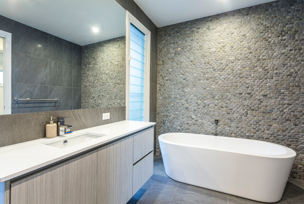 This is an example of a contemporary master bathroom in Brisbane with light wood cabinets, a freestanding tub, stone tile and granite benchtops.