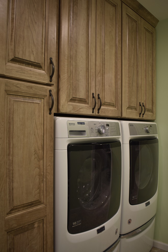 Design ideas for a large traditional u-shaped laundry room in St Louis with an undermount sink, raised-panel cabinets, brown cabinets, quartzite benchtops, brown splashback, travertine splashback, vinyl floors, brown floor and white benchtop.