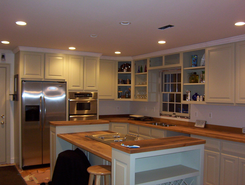 Large transitional l-shaped enclosed kitchen photo in DC Metro with a double-bowl sink, raised-panel cabinets, green cabinets, wood countertops, white backsplash, stainless steel appliances and an island