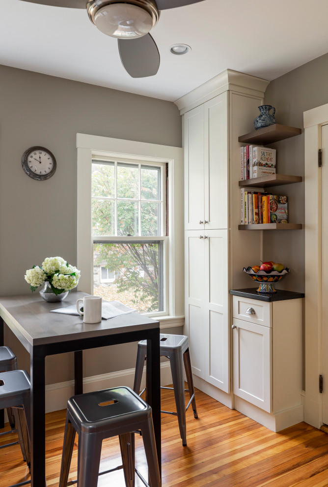 Mid-sized transitional galley light wood floor kitchen pantry photo in Boston with a farmhouse sink, shaker cabinets, white cabinets, granite countertops, gray backsplash, subway tile backsplash, stainless steel appliances, no island and black countertops