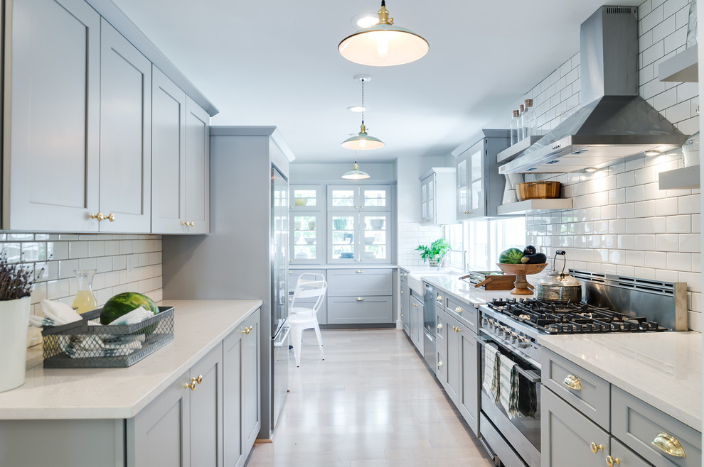 Photo of a transitional galley kitchen in Philadelphia with a farmhouse sink, shaker cabinets, grey cabinets, white splashback, subway tile splashback, stainless steel appliances, no island and beige floor.