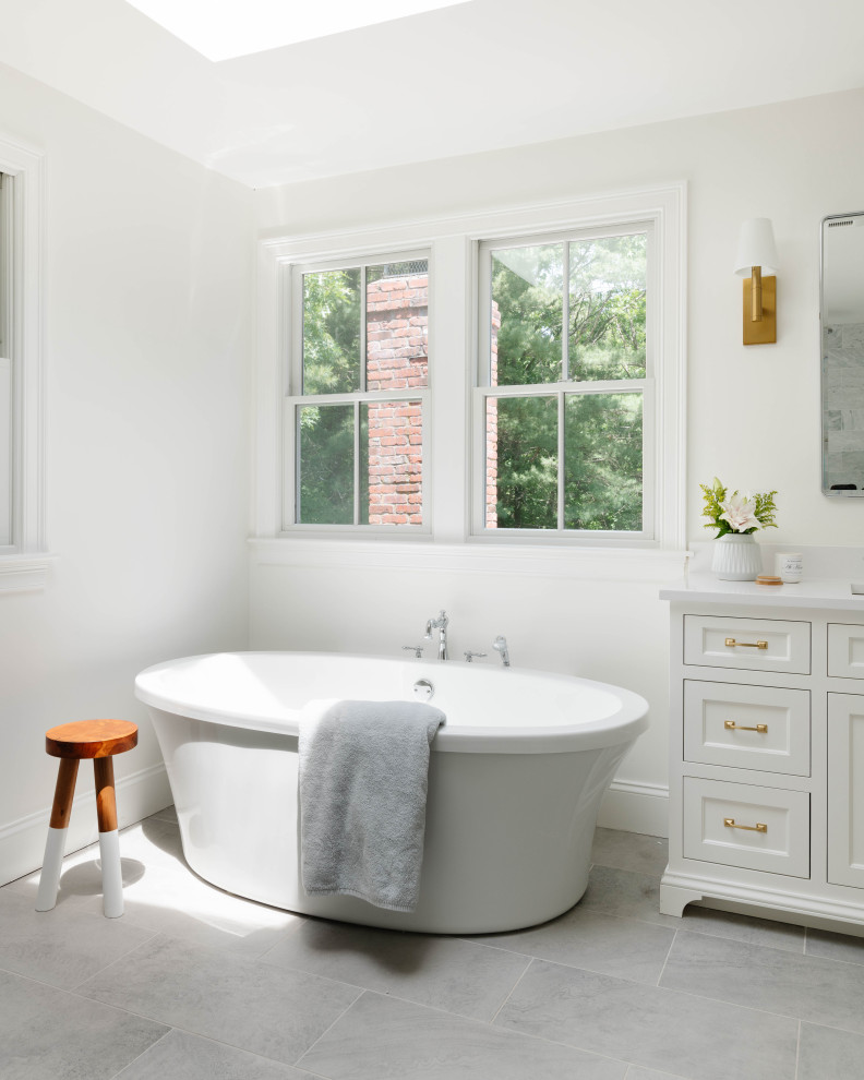 Photo of a large classic bathroom in Boston with white cabinets, a built in vanity unit, engineered stone worktops, double sinks, a freestanding bath, white worktops, white walls, a submerged sink, recessed-panel cabinets, porcelain flooring and grey floors.