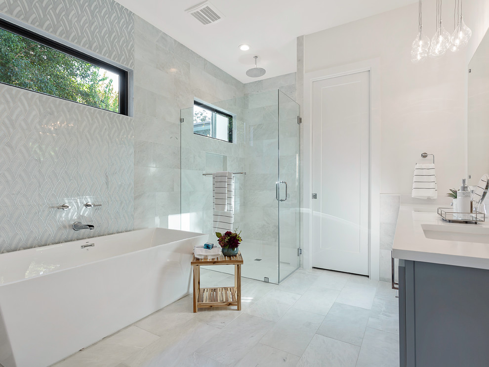 Photo of a large contemporary master bathroom in Austin with flat-panel cabinets, grey cabinets, a freestanding tub, a curbless shower, a two-piece toilet, gray tile, ceramic tile, white walls, ceramic floors, an undermount sink, engineered quartz benchtops, grey floor, a hinged shower door and white benchtops.