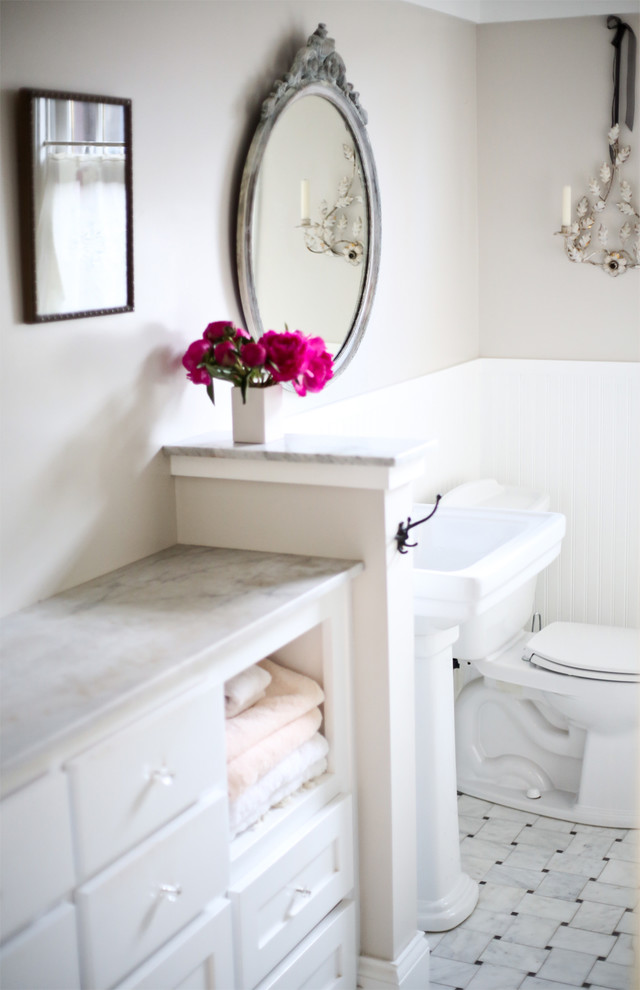 Photo of a small traditional bathroom in San Francisco with flat-panel cabinets, white cabinets, a two-piece toilet, white walls, ceramic floors, a pedestal sink, marble benchtops and white floor.