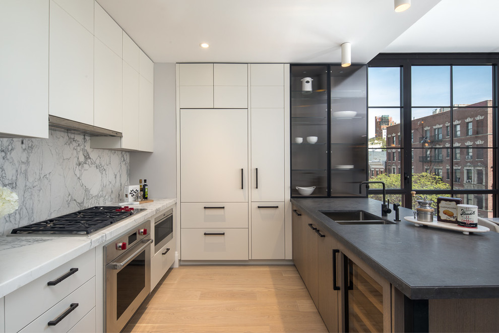 Photo of a mid-sized contemporary kitchen in New York with white cabinets, marble benchtops, a double-bowl sink, flat-panel cabinets, white splashback, marble splashback, stainless steel appliances, light hardwood floors and a peninsula.