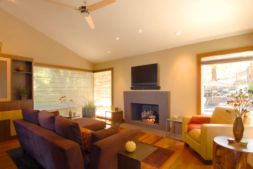 This is an example of a contemporary family room in San Francisco with beige walls, medium hardwood floors, a standard fireplace and a wall-mounted tv.