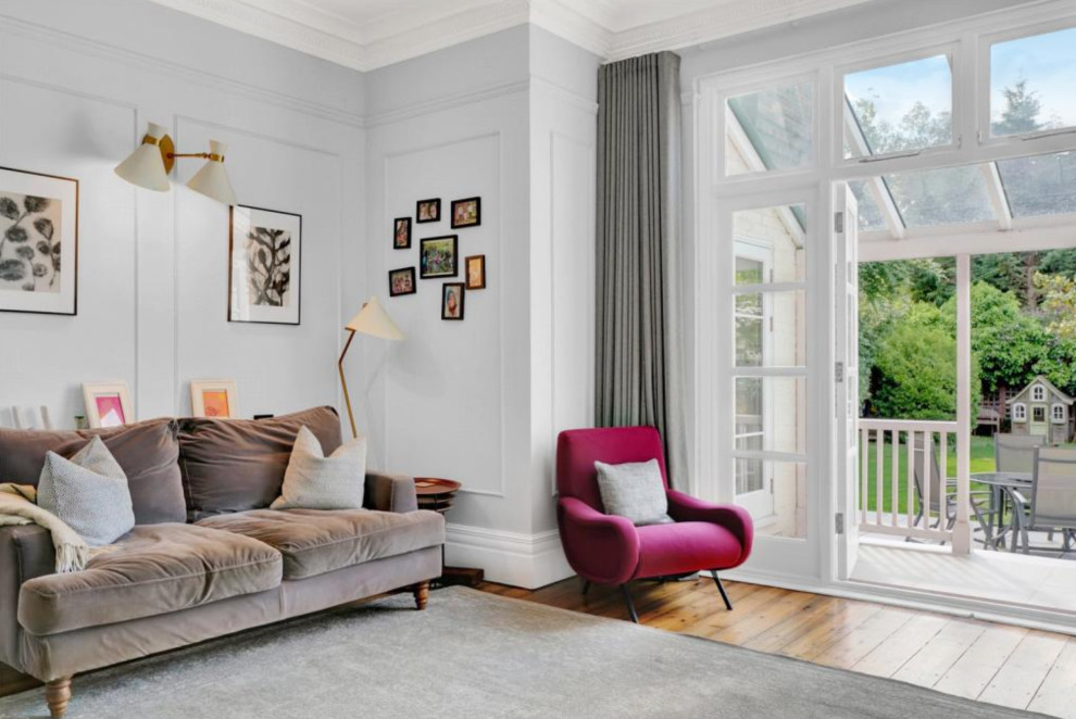 Large contemporary enclosed living room in London with grey walls, light hardwood floors, a standard fireplace, a metal fireplace surround, a corner tv, beige floor and panelled walls.