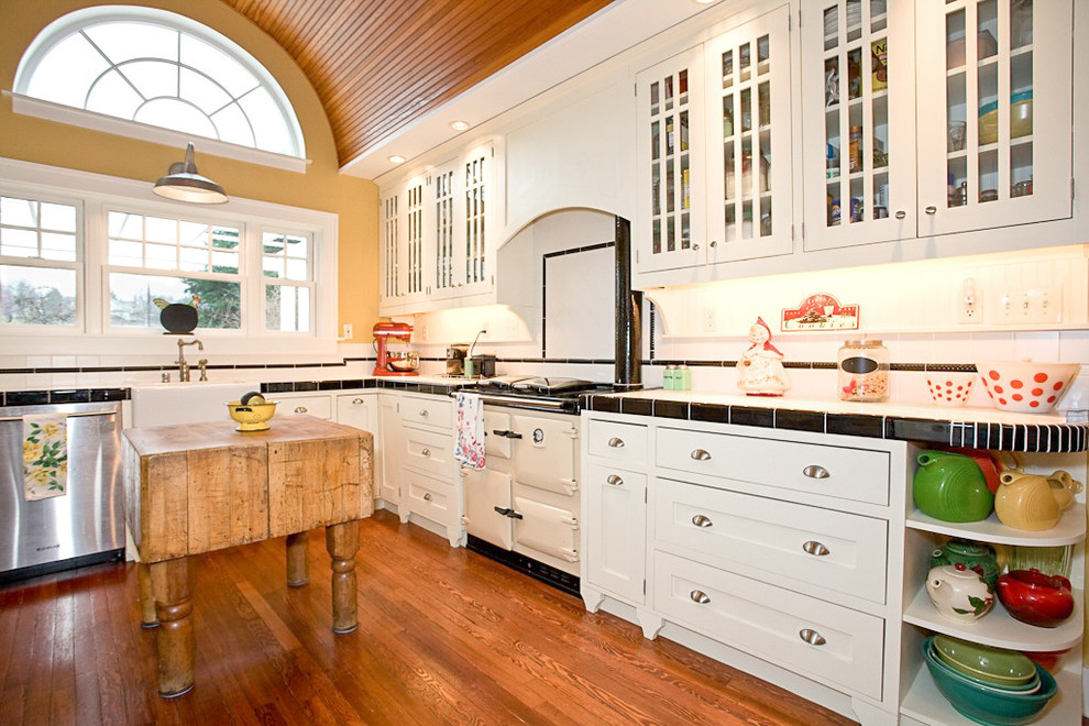 This is an example of a country l-shaped kitchen in Seattle with a farmhouse sink, shaker cabinets, white cabinets, white splashback, dark hardwood floors and with island.