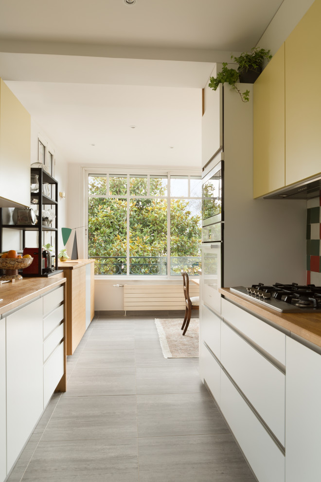 Large tropical galley open plan kitchen in Paris with an undermount sink, white cabinets, wood benchtops, multi-coloured splashback, terra-cotta splashback, stainless steel appliances, terra-cotta floors, no island and grey floor.
