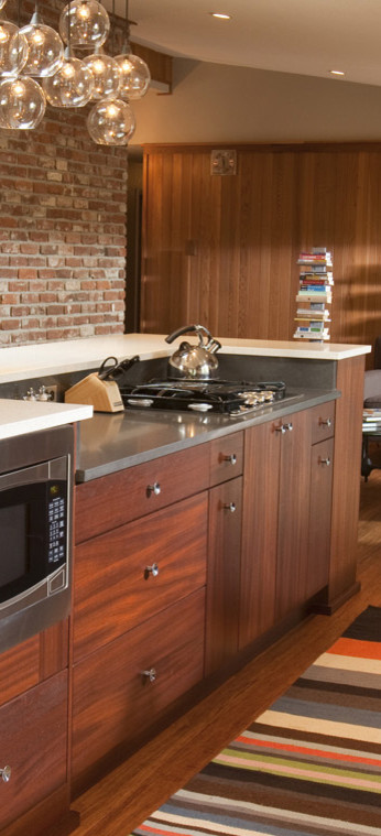 Photo of a mid-sized midcentury single-wall eat-in kitchen in Portland with an undermount sink, flat-panel cabinets, dark wood cabinets, quartz benchtops, beige splashback, porcelain splashback, stainless steel appliances, medium hardwood floors, with island, brown floor, multi-coloured benchtop and vaulted.