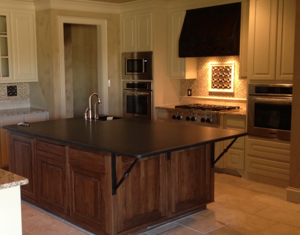 Eat-in kitchen - mid-sized rustic galley travertine floor eat-in kitchen idea in Austin with an undermount sink, raised-panel cabinets, medium tone wood cabinets, granite countertops, beige backsplash, stone tile backsplash, stainless steel appliances and an island