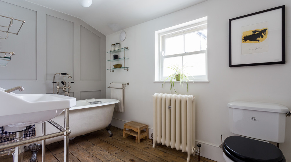 This is an example of a mid-sized traditional master bathroom in London with a claw-foot tub, white walls, a console sink, a two-piece toilet and medium hardwood floors.