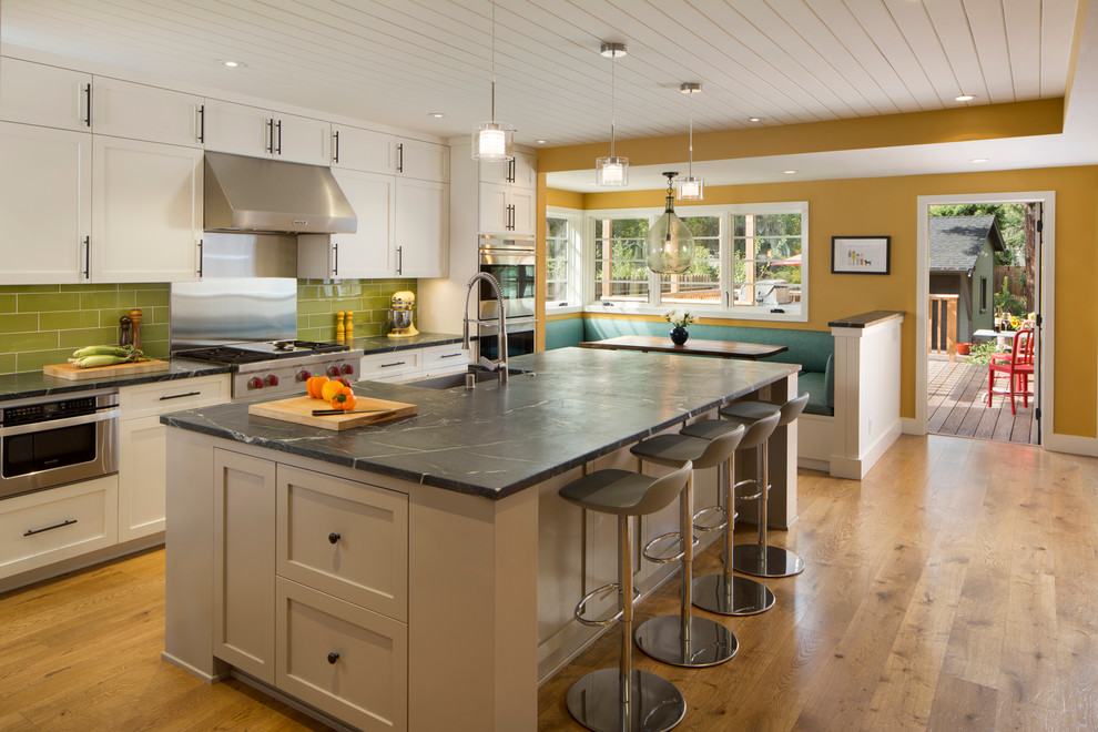 Inspiration for a large arts and crafts eat-in kitchen in San Francisco with soapstone benchtops, green splashback, stainless steel appliances, medium hardwood floors, with island, a farmhouse sink, brown floor, recessed-panel cabinets, grey cabinets and glass tile splashback.