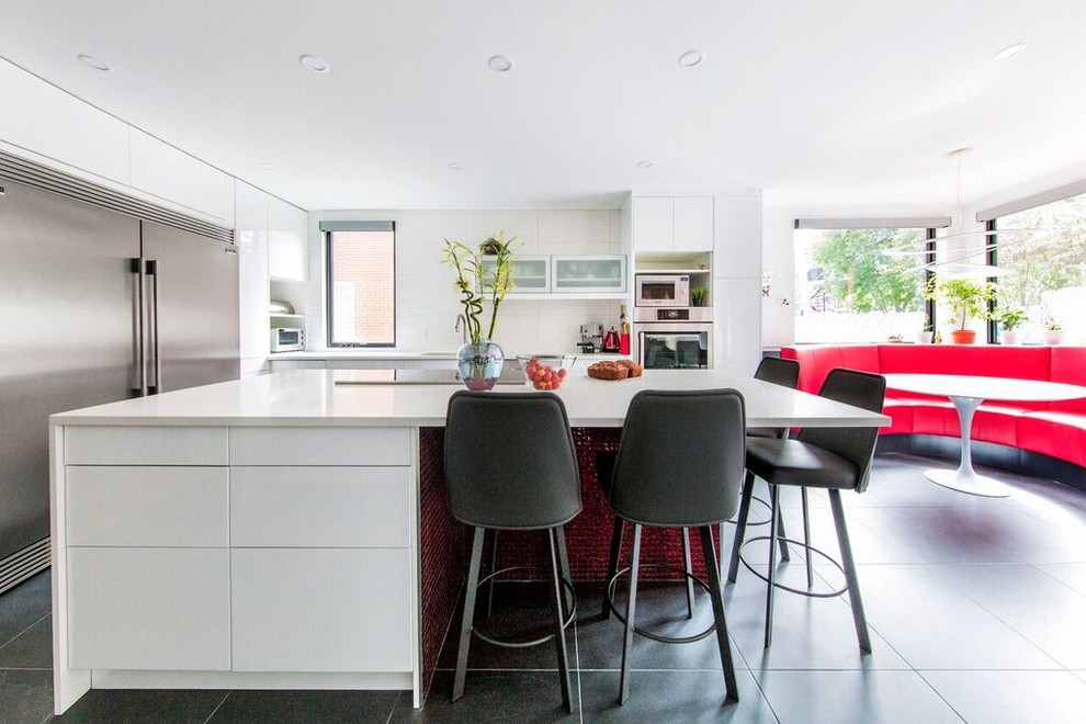 This is an example of a contemporary eat-in kitchen in Montreal with flat-panel cabinets, white cabinets, white splashback, stainless steel appliances, with island, black floor and white benchtop.