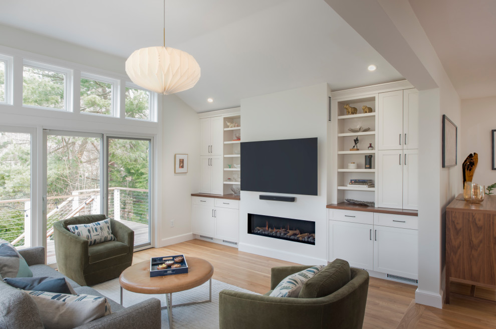 This is an example of a transitional open concept family room in Boston with white walls, medium hardwood floors, a wall-mounted tv, brown floor and vaulted.