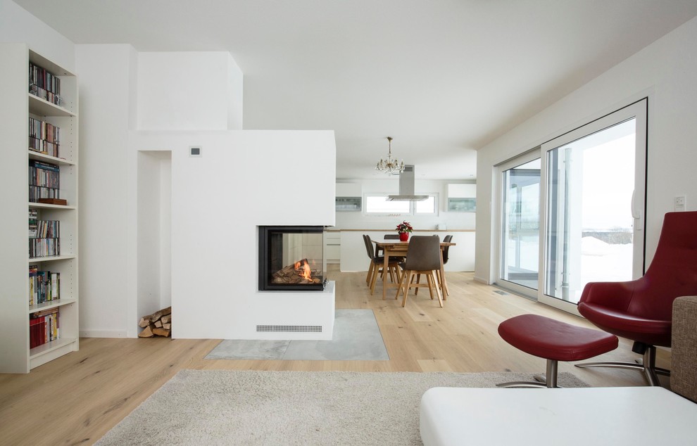Photo of a large contemporary open concept living room in Stuttgart with white walls, light hardwood floors, a two-sided fireplace, a plaster fireplace surround, a library, no tv and beige floor.
