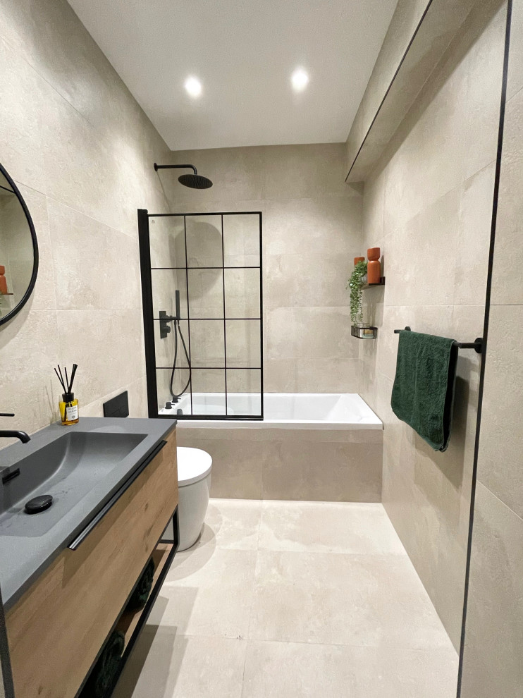 Mid-sized modern kids bathroom in Hertfordshire with flat-panel cabinets, medium wood cabinets, a drop-in tub, a shower/bathtub combo, a two-piece toilet, beige tile, porcelain tile, beige walls, porcelain floors, an integrated sink, beige floor, a hinged shower door, black benchtops, a single vanity and a floating vanity.
