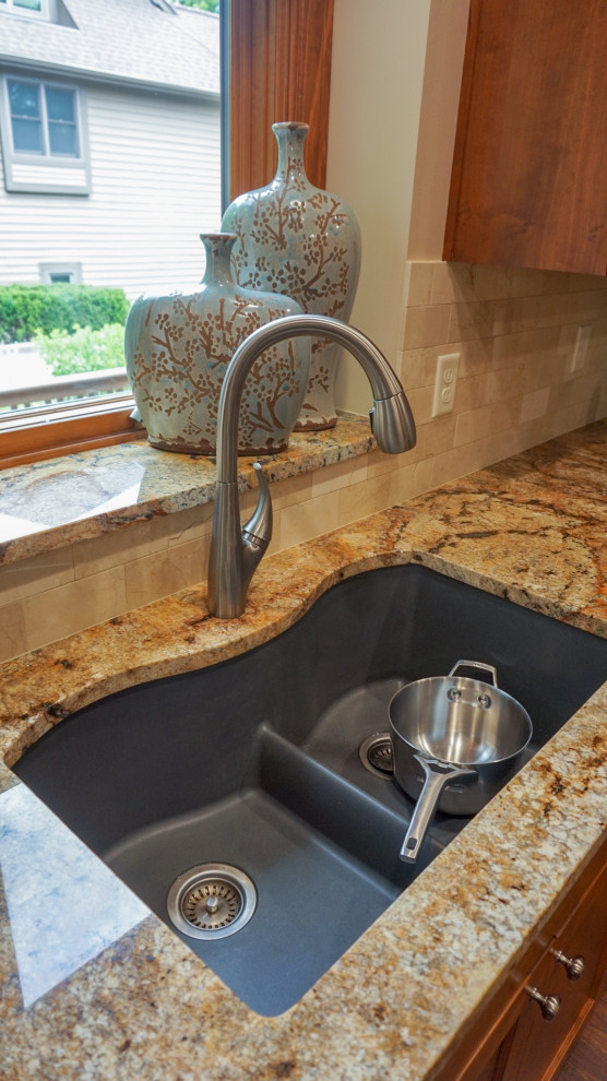 Example of a mid-sized u-shaped laminate floor enclosed kitchen design with a double-bowl sink, recessed-panel cabinets, medium tone wood cabinets, granite countertops, beige backsplash, ceramic backsplash, stainless steel appliances and an island