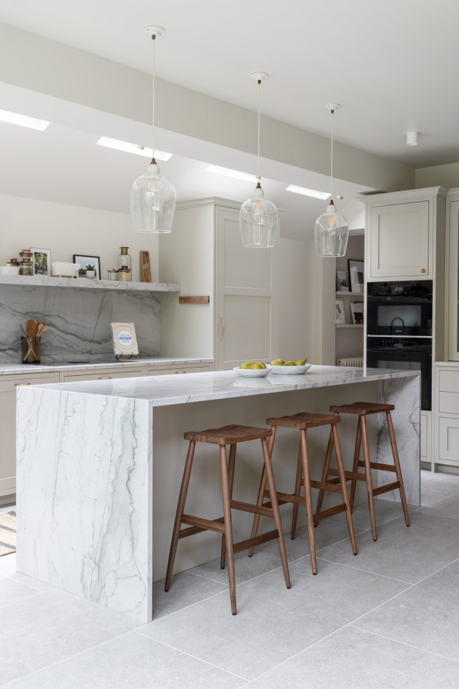 Photo of a medium sized contemporary l-shaped kitchen/diner in London with shaker cabinets, beige cabinets, marble worktops, black appliances, a breakfast bar, a vaulted ceiling and feature lighting.