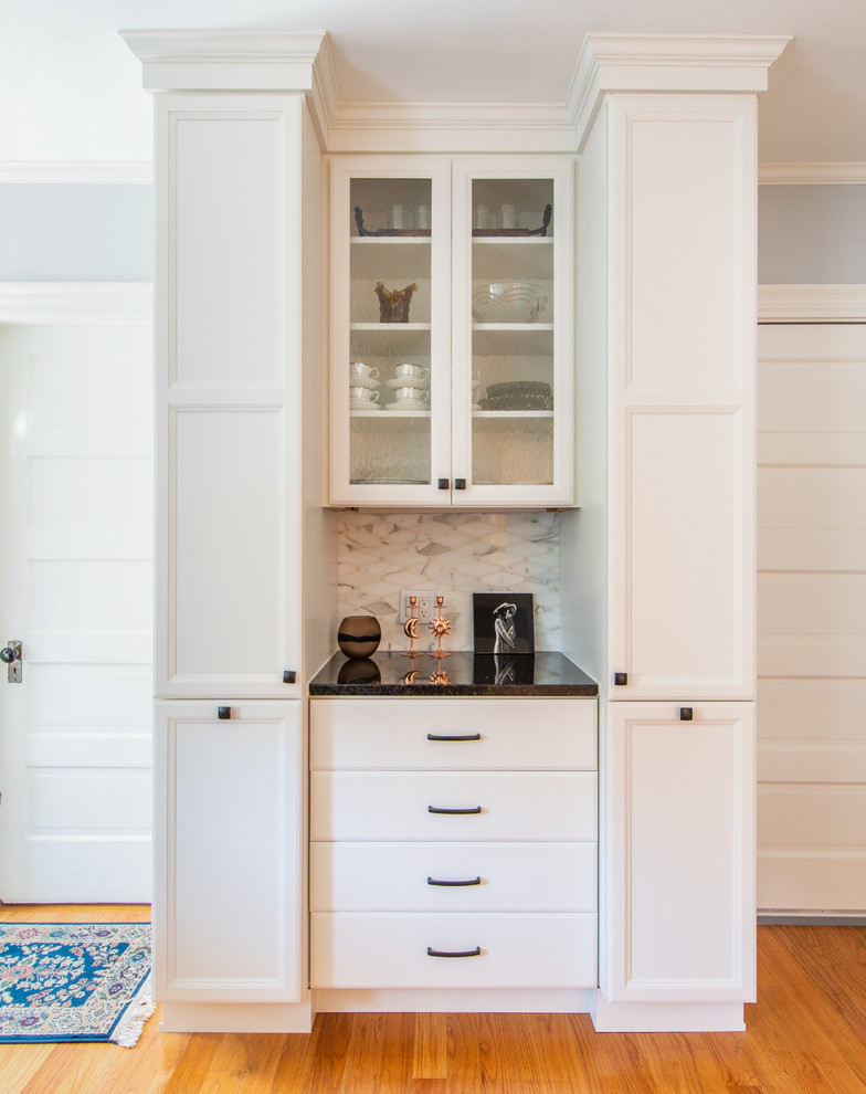 This is an example of a small traditional l-shaped separate kitchen in Boston with an undermount sink, recessed-panel cabinets, white cabinets, granite benchtops, grey splashback, glass tile splashback, stainless steel appliances, light hardwood floors, no island, brown floor and black benchtop.
