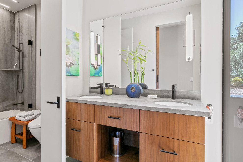 Photo of a mid-sized modern kids bathroom in San Francisco with flat-panel cabinets, brown cabinets, an open shower, a one-piece toilet, beige tile, limestone, white walls, ceramic floors, an undermount sink, limestone benchtops, grey floor, an open shower, beige benchtops, a double vanity and a floating vanity.