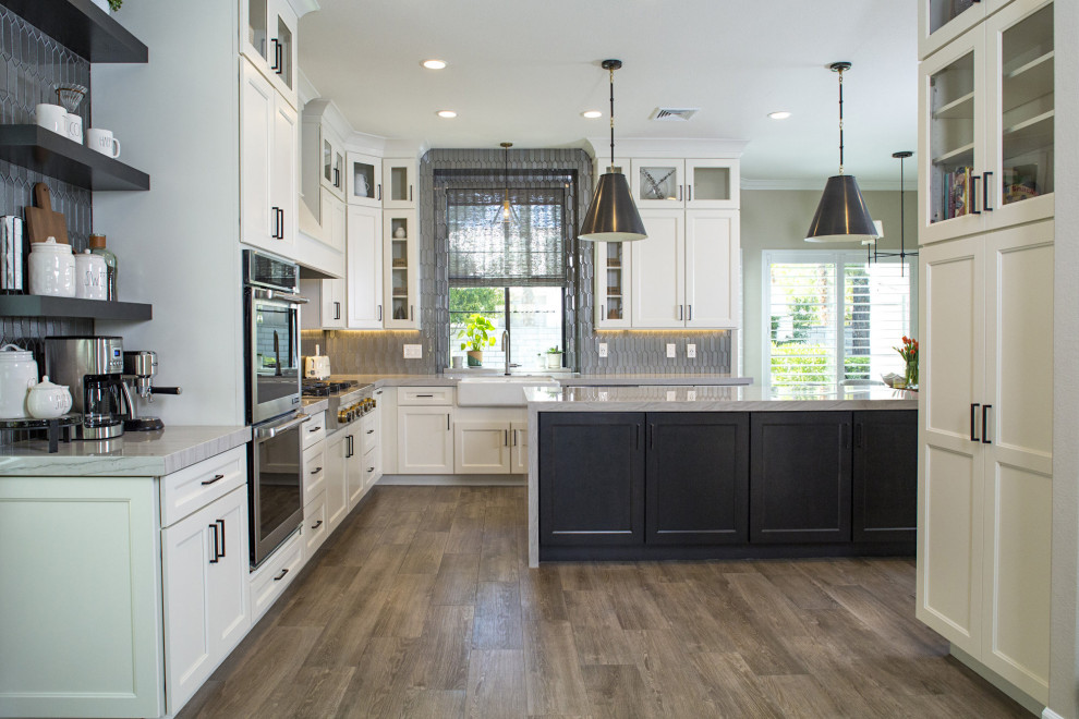Large mid-century modern l-shaped porcelain tile and brown floor eat-in kitchen photo in Las Vegas with a farmhouse sink, raised-panel cabinets, white cabinets, quartzite countertops, gray backsplash, glass tile backsplash, stainless steel appliances, an island and beige countertops