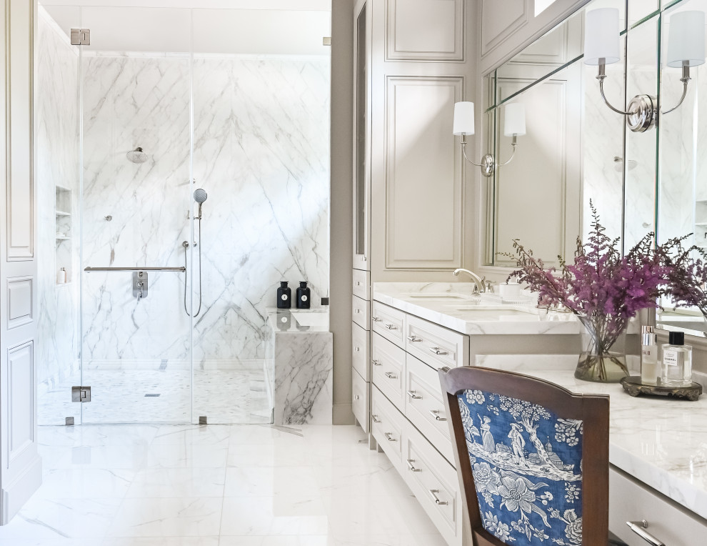Cette image montre une grande salle de bain principale traditionnelle avec un placard avec porte à panneau surélevé, des portes de placard beiges, une baignoire encastrée, un espace douche bain, WC séparés, un carrelage gris, du carrelage en marbre, un mur beige, un sol en marbre, un lavabo encastré, un plan de toilette en marbre, un sol blanc, une cabine de douche à porte battante, un plan de toilette blanc, meuble simple vasque, meuble-lavabo encastré et du lambris.