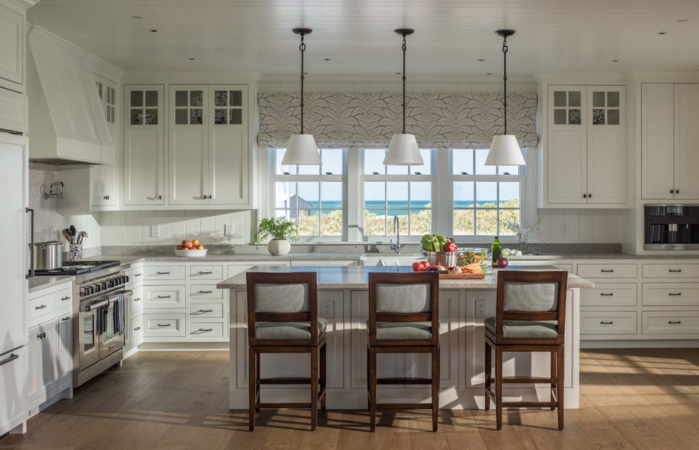Photo of a beach style kitchen in Boston with a farmhouse sink, shaker cabinets, white cabinets, granite benchtops, panelled appliances, medium hardwood floors and with island.