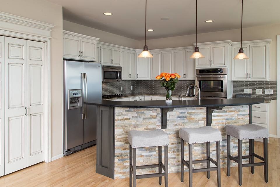 Inspiration for a mid-sized transitional l-shaped open plan kitchen in Milwaukee with raised-panel cabinets, white cabinets, quartz benchtops, black splashback, porcelain splashback, stainless steel appliances, light hardwood floors, with island and beige floor.