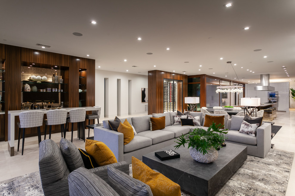 Expansive contemporary open concept family room in Orange County with a home bar, white walls, marble floors and beige floor.