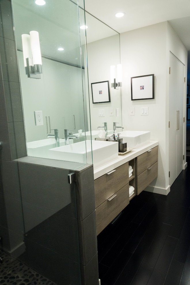 Design ideas for a mid-sized modern master bathroom in Los Angeles with flat-panel cabinets, distressed cabinets, an alcove shower, a wall-mount toilet, black tile, porcelain tile, black walls, dark hardwood floors, a vessel sink, solid surface benchtops, black floor and a hinged shower door.