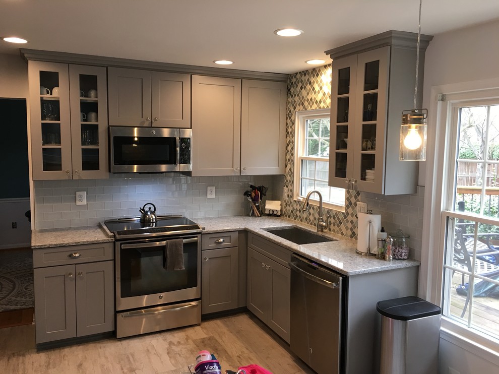 Design ideas for a mid-sized transitional l-shaped kitchen in DC Metro with an undermount sink, shaker cabinets, grey cabinets, granite benchtops, grey splashback, subway tile splashback, stainless steel appliances, light hardwood floors, no island and brown floor.