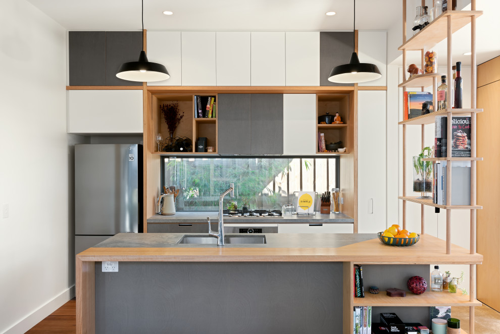 Mid-sized contemporary galley open plan kitchen in Melbourne with an undermount sink, flat-panel cabinets, window splashback, stainless steel appliances, with island, grey benchtop, white cabinets, medium hardwood floors and brown floor.