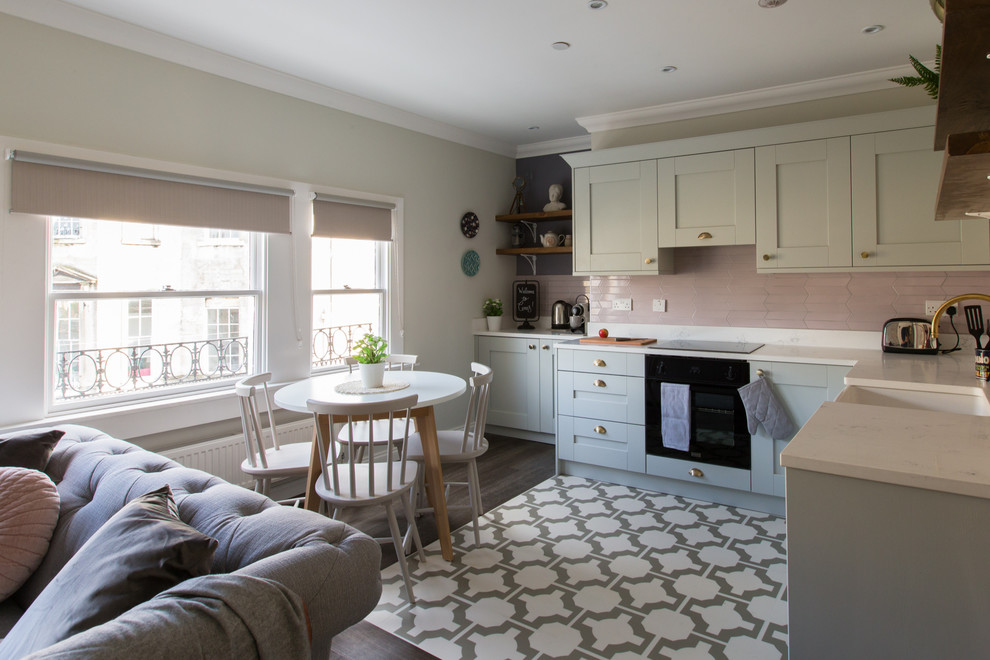 Mid-sized l-shaped eat-in kitchen in Sussex with a farmhouse sink, shaker cabinets, grey cabinets, solid surface benchtops, pink splashback, ceramic splashback, black appliances, vinyl floors and no island.