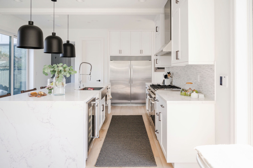 Photo of a mid-sized modern galley eat-in kitchen in San Francisco with a drop-in sink, shaker cabinets, white cabinets, marble benchtops, white splashback, matchstick tile splashback, stainless steel appliances, light hardwood floors, with island, brown floor, grey benchtop and exposed beam.