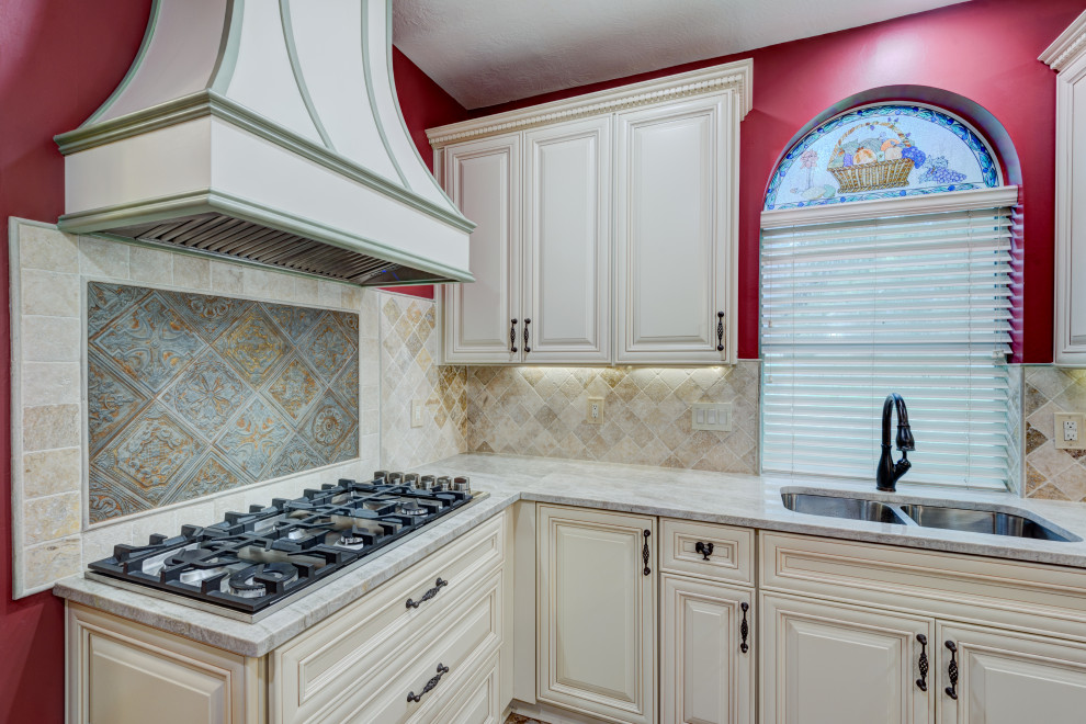 Foto på ett mellanstort beige kök, med en dubbel diskho, luckor med upphöjd panel, vita skåp, granitbänkskiva, beige stänkskydd, stänkskydd i travertin, rostfria vitvaror, tegelgolv, en köksö och beiget golv