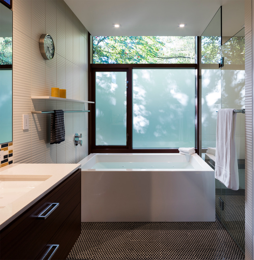 Photo of a modern master bathroom in Seattle with flat-panel cabinets, medium wood cabinets, a freestanding tub, a curbless shower, black tile, porcelain tile, white walls, an undermount sink and solid surface benchtops.