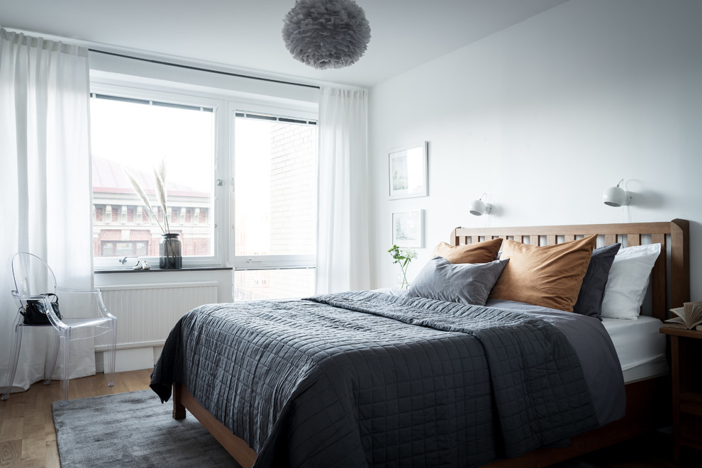 Photo of a scandinavian bedroom in Gothenburg with white walls, medium hardwood floors and brown floor.