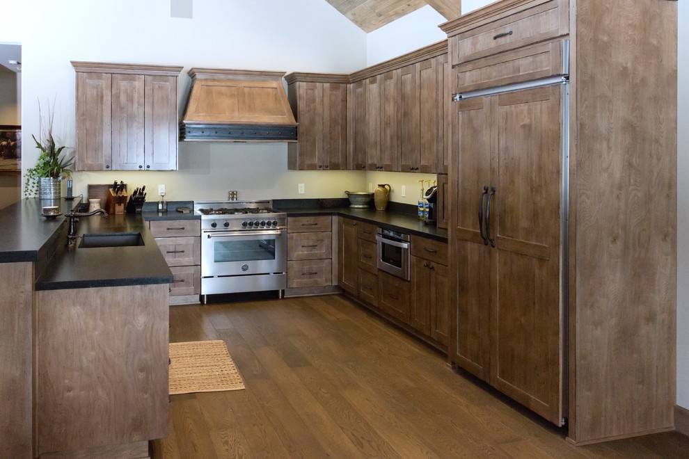 Example of a large mountain style u-shaped medium tone wood floor and brown floor open concept kitchen design in Phoenix with an undermount sink, shaker cabinets, medium tone wood cabinets, solid surface countertops, paneled appliances, no island and black countertops
