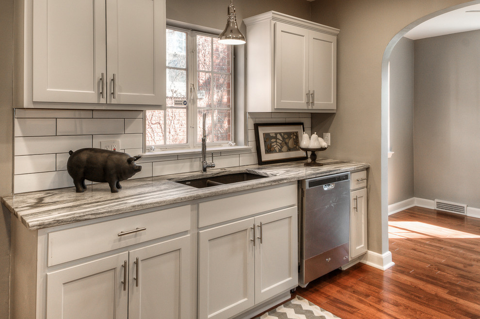 This is an example of a contemporary galley eat-in kitchen in Houston with an undermount sink, recessed-panel cabinets, white cabinets, quartz benchtops, white splashback, ceramic splashback, stainless steel appliances, medium hardwood floors and no island.