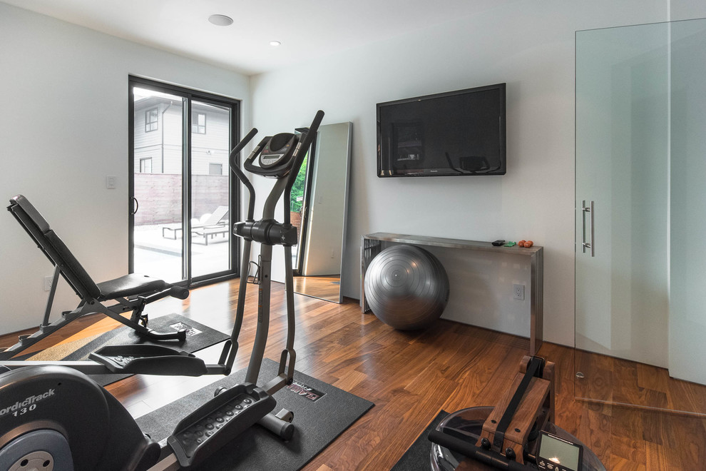Photo of a small midcentury home gym in Vancouver with white walls, medium hardwood floors and brown floor.