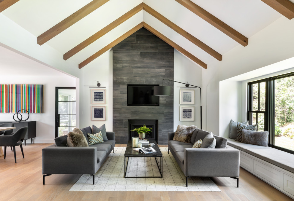 Design ideas for a large contemporary open plan games room in New York with white walls, light hardwood flooring, a standard fireplace, a tiled fireplace surround, a wall mounted tv, brown floors and exposed beams.