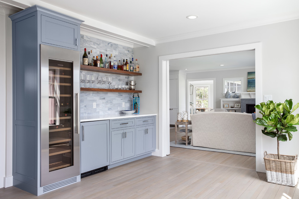 Beach style single-wall home bar in Boston with shaker cabinets, blue cabinets, grey splashback, light hardwood floors, beige floor and white benchtop.