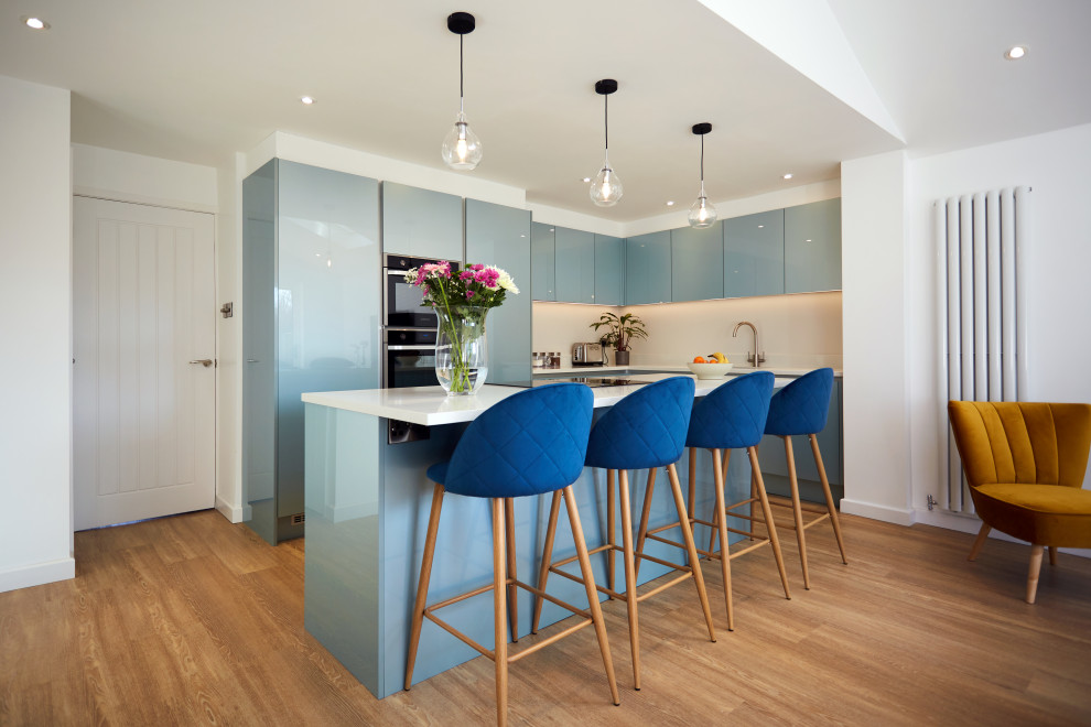 Exemple d'une cuisine tendance en L avec un placard à porte plane, des portes de placard bleues, un électroménager noir, un sol en bois brun, îlot, un sol marron et un plan de travail blanc.