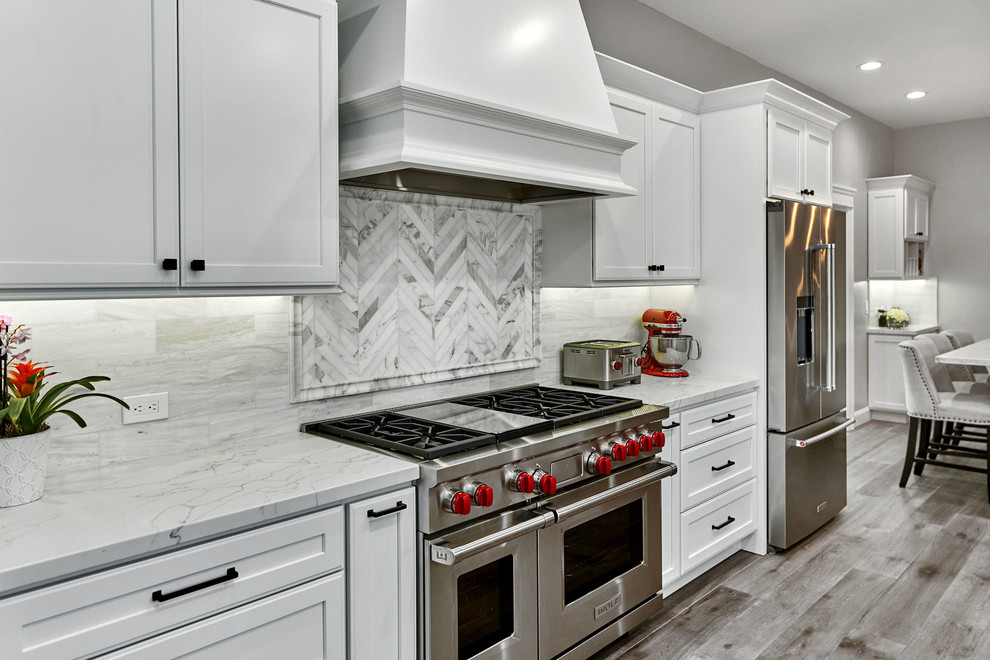 This is an example of a mid-sized transitional galley eat-in kitchen in San Francisco with an undermount sink, flat-panel cabinets, white cabinets, quartz benchtops, white splashback, marble splashback, stainless steel appliances, light hardwood floors, with island, grey floor and white benchtop.