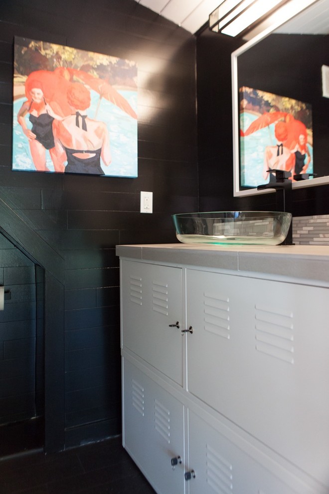 This is an example of a mid-sized eclectic 3/4 bathroom in Portland with furniture-like cabinets, white cabinets, an alcove tub, a two-piece toilet, gray tile, white tile, matchstick tile, black walls, a vessel sink, solid surface benchtops, black floor and laminate floors.