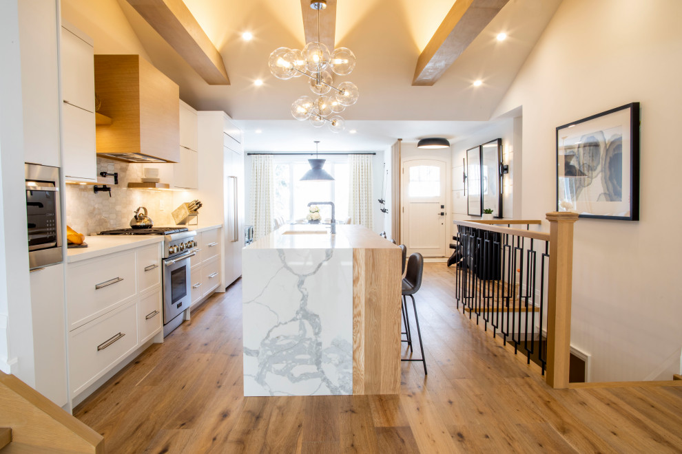 Inspiration for a mid-sized contemporary u-shaped eat-in kitchen in Toronto with an undermount sink, flat-panel cabinets, white cabinets, quartzite benchtops, white splashback, marble splashback, stainless steel appliances, light hardwood floors, with island, brown floor and white benchtop.