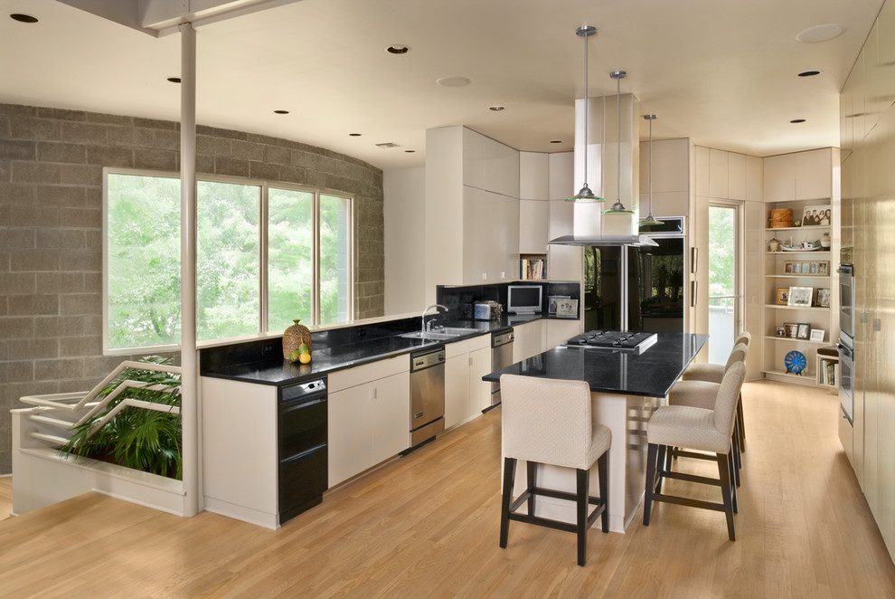 Design ideas for a contemporary kitchen in New Orleans with flat-panel cabinets, black splashback, light hardwood floors, with island, an undermount sink and stainless steel appliances.